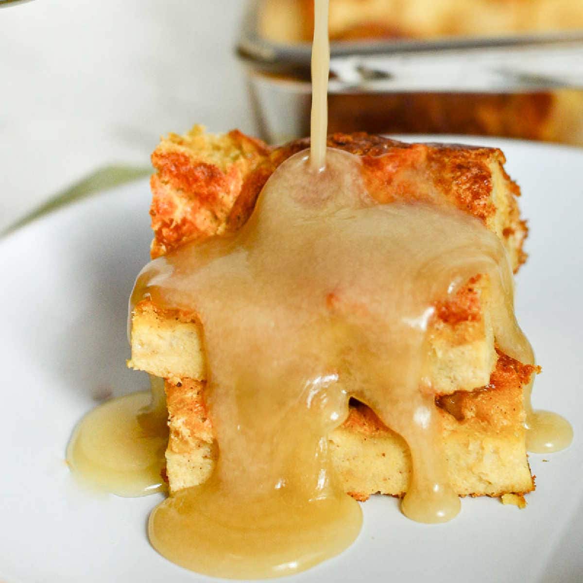 white plate filled with two slices of old fashioned bread pudding and drizzled with vanilla sauce.