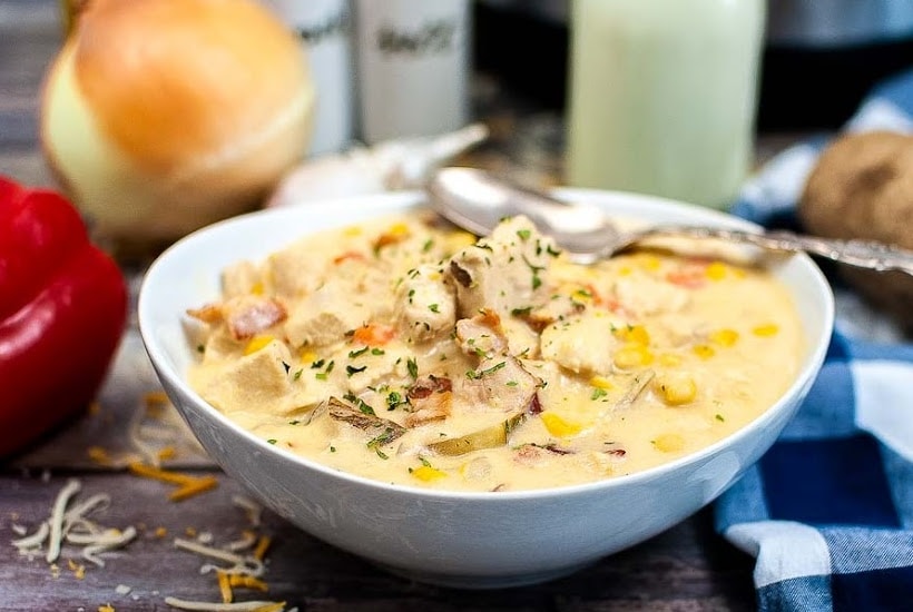 A white filled with bowl chicken corn chowder with a spoon on the side.