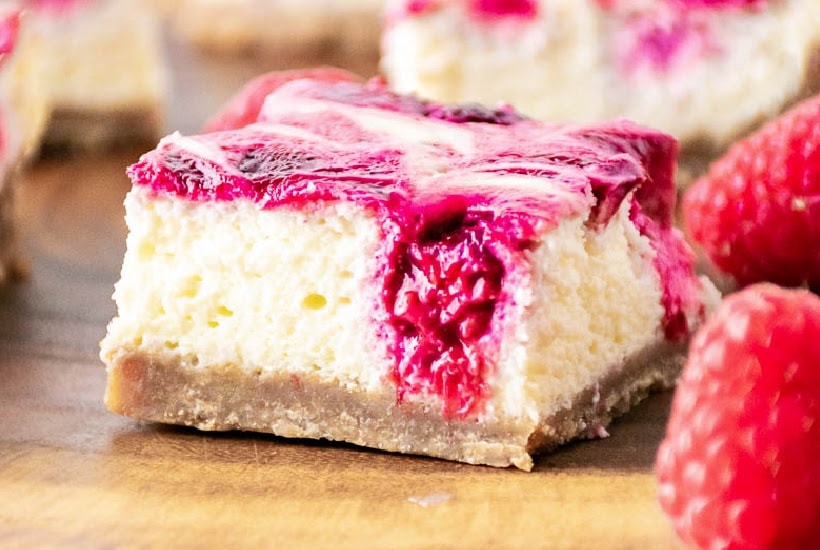 Front closeup of a slice of a Cheesecake Bar with Raspberry Swirl next to fresh raspberries.