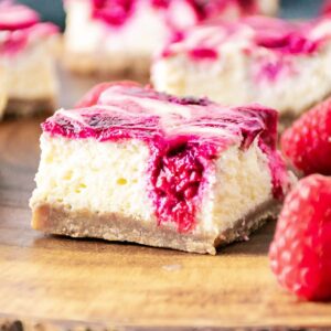 Raspberry Cheesecake Bars on a wooden cutting board next to raspberries.