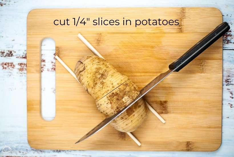 a potato sitting between two chopsticks and being cut in the hasselback technique.