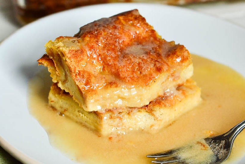 two slices of bread pudding with vanilla sauce on a white plate.