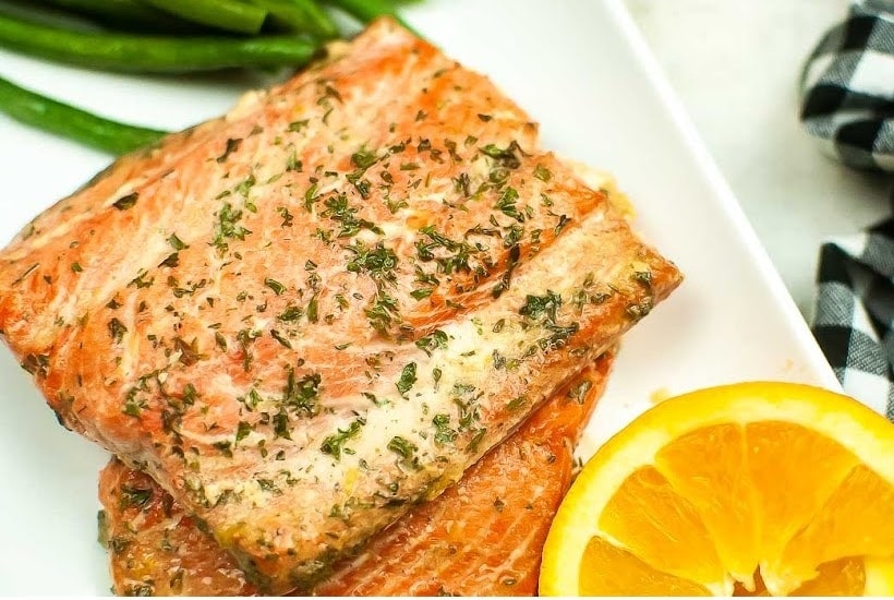 top close up view of air fryer honey orange glazed salmon next to orange slices.