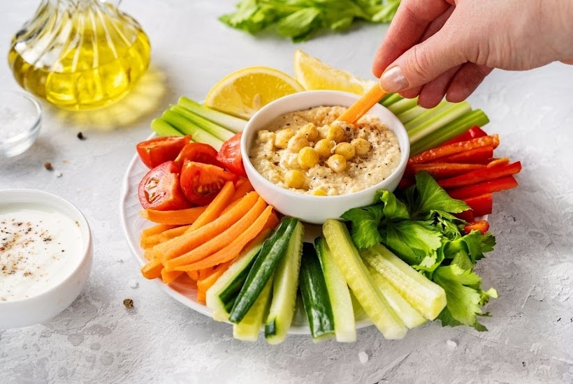 white plate filled with cut vegetables and bowl of hummus dip.