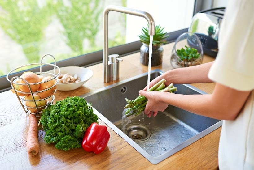 woman rinsing asparagus and other veggies at the sink.
