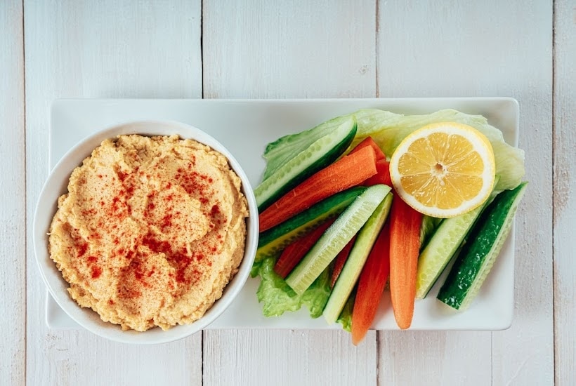 white platter filled with cut vegetables and bowl of hummus for dipping.