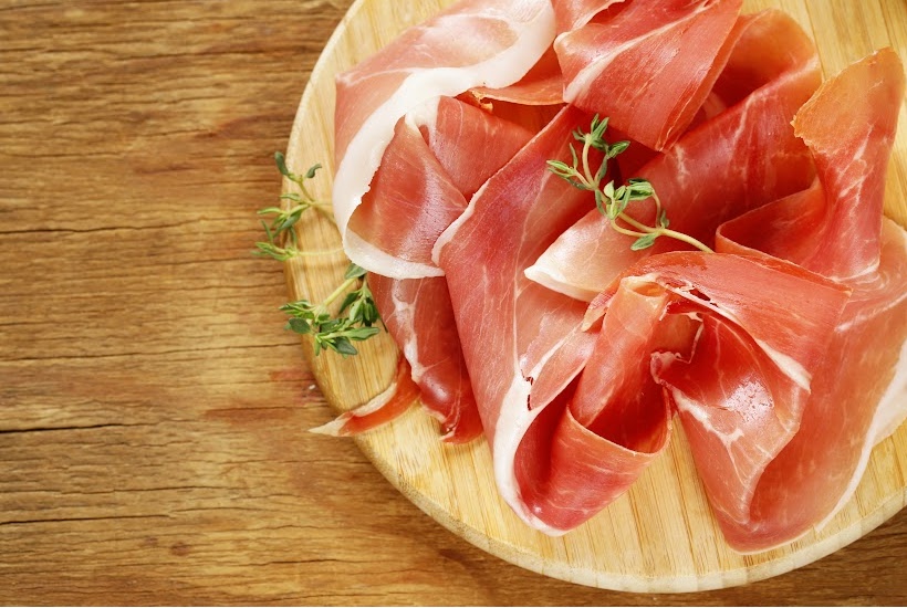 very thin slices of ham on a round wooden cutting board.