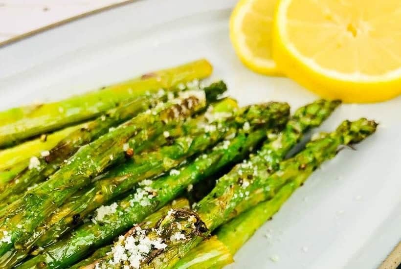 Closeup view of cooked asparagus on a white platter with lemon slices.
