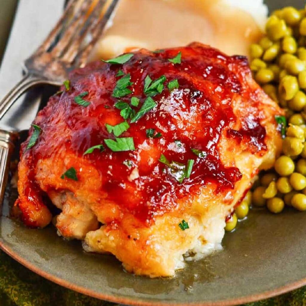 Front view of BBQ Baked Chicken Thighs on a plate with peas and a fork.