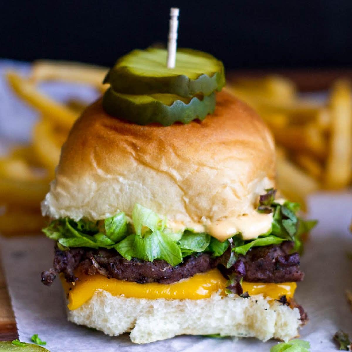 Front closeup view of a Big Mac Slider with pickles on top on parchment paper.