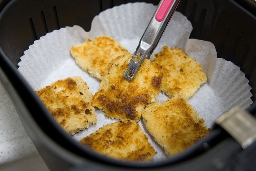 picking up breaded food on a parchment paper lined air fryer basket.