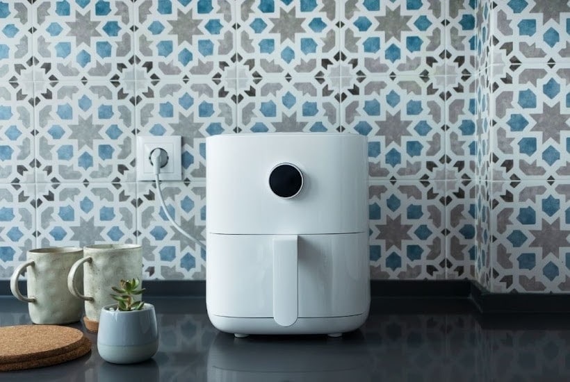 whit air fryer on a counter with 2 mugs and small potted plant.