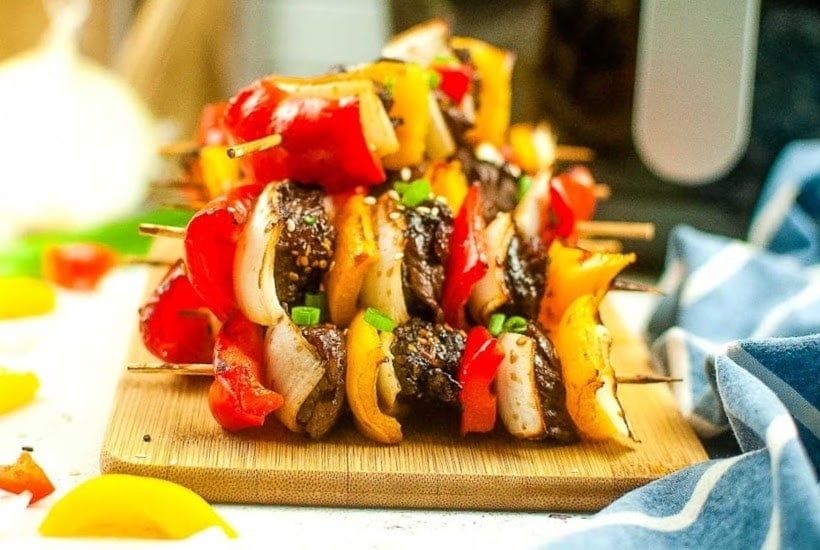Air fryer beef kabobs stacked on a cutting board.