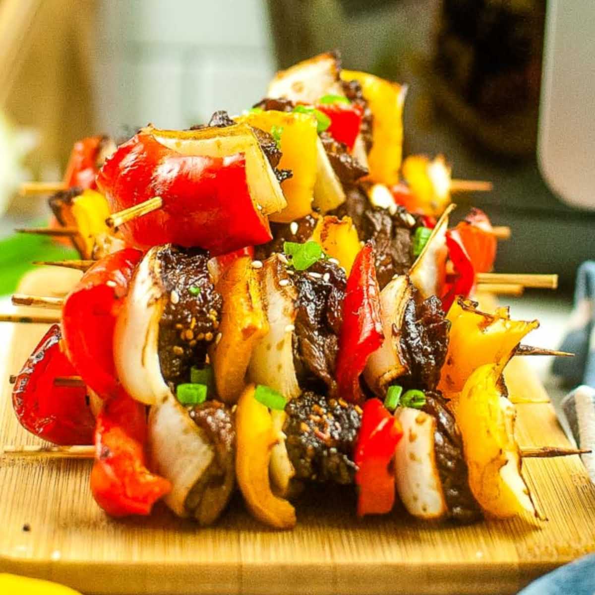 Close up of a cutting board with air fryer beef kabobs stacked on each other.