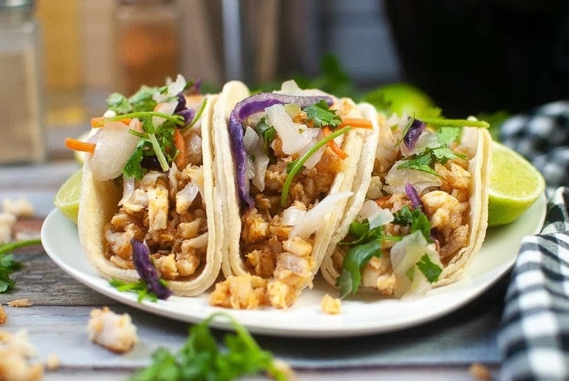 Front view of air fryer fish tacos on a white plate with lime garnish.