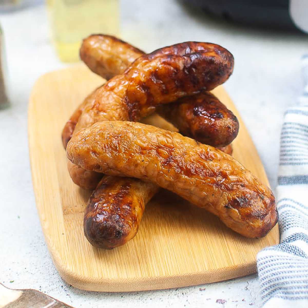 Front view of air fried Italian sausages stacked on a wooden cutting board.