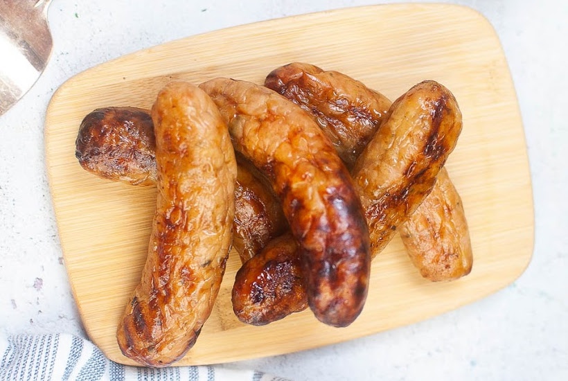 Overhead view of air fried Italian sausages on a wood cutting board.