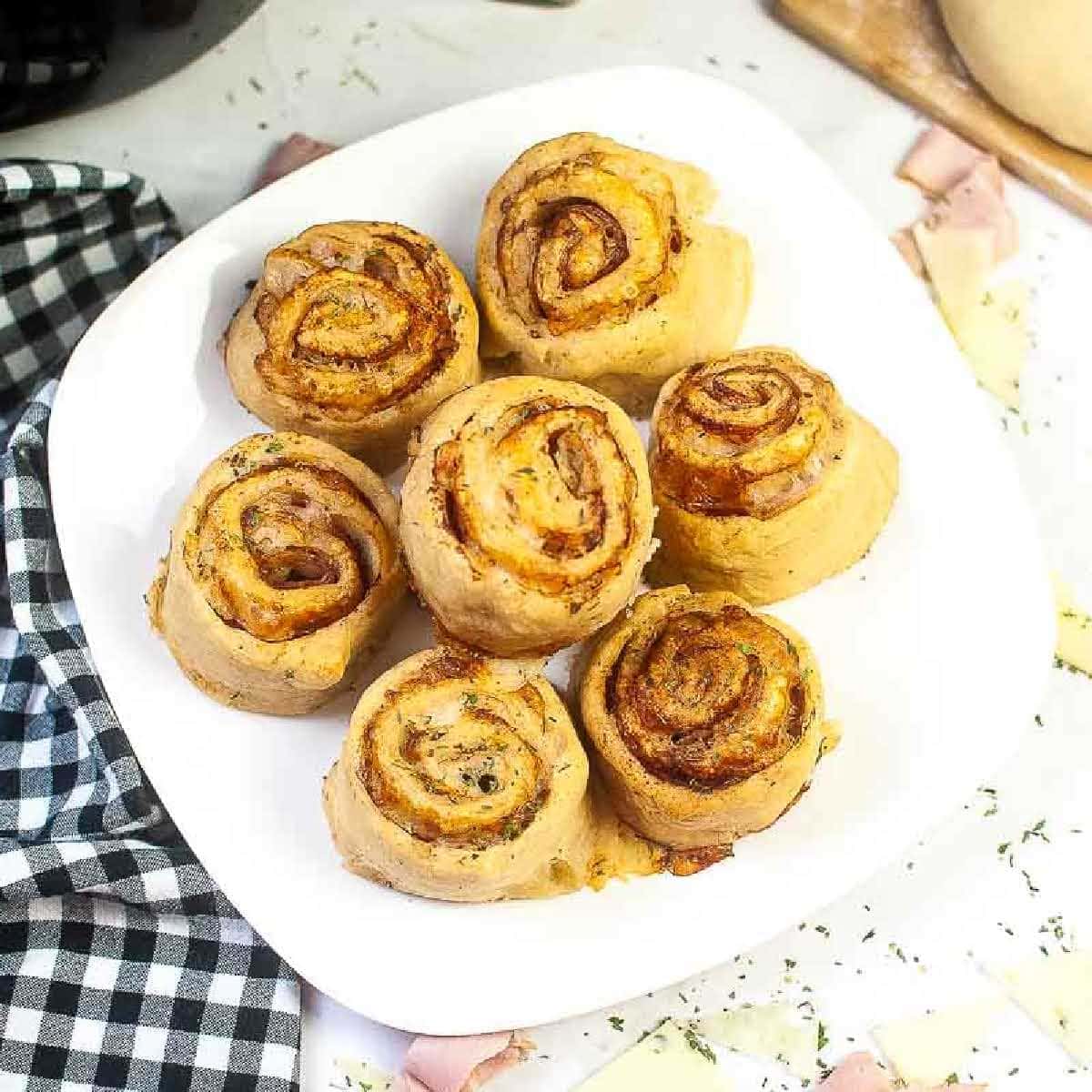 Top view of air fryer ham and cheese pinwheels on a white plate with a black and white checked napkin in the background.