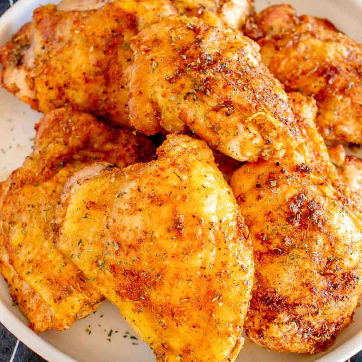 Front view of Southern baked chicken thighs stacked on a white plate.