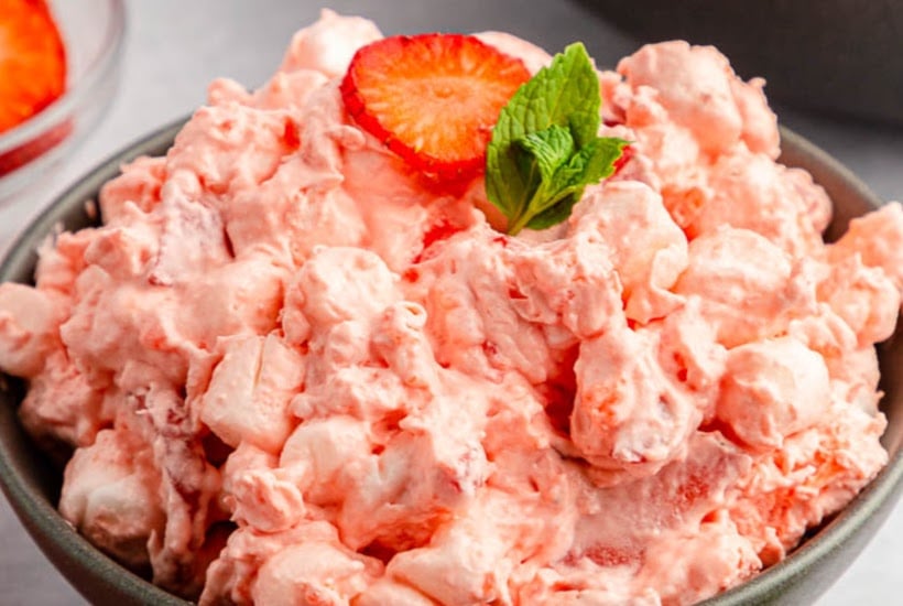 Closeup view of serving bowl filled with strawberry fluff jello salad garnished with a slice of strawberry and mint.