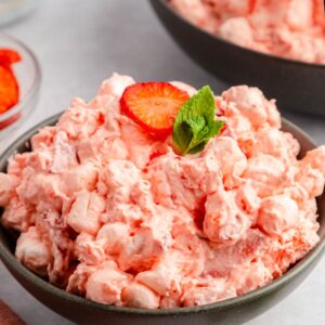 Front close up of Strawberry Fluff Salad in a serving bowl garnished with a slice of strawberry and mint.