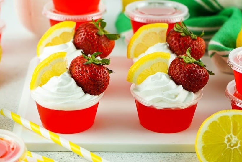 Front view of strawberry lemonade jello shots topped with whipped topping, strawberry and lemon slice.