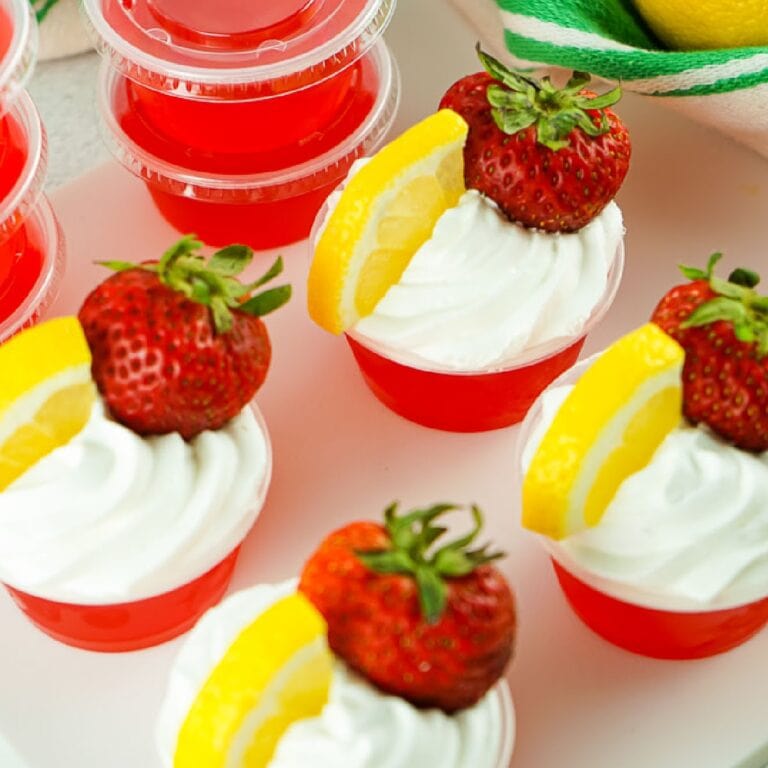 Overhead view of four Strawberry Lemonade Jello Shots with whipped topping, lemon slices, and strawberry.
