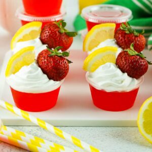 Front view of Strawberry Lemonade Jello Shots garnished with whipped topping and slices of lemons and strawberries.