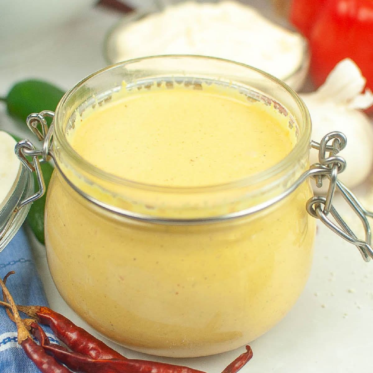 Closeup view of glass jar filled with copycat Taco Bell Baja sauce with red chile peppers in front.