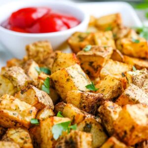 Closeup view of seasoned air fried diced potatoes on a white platter with a bowl of dipping sauce.