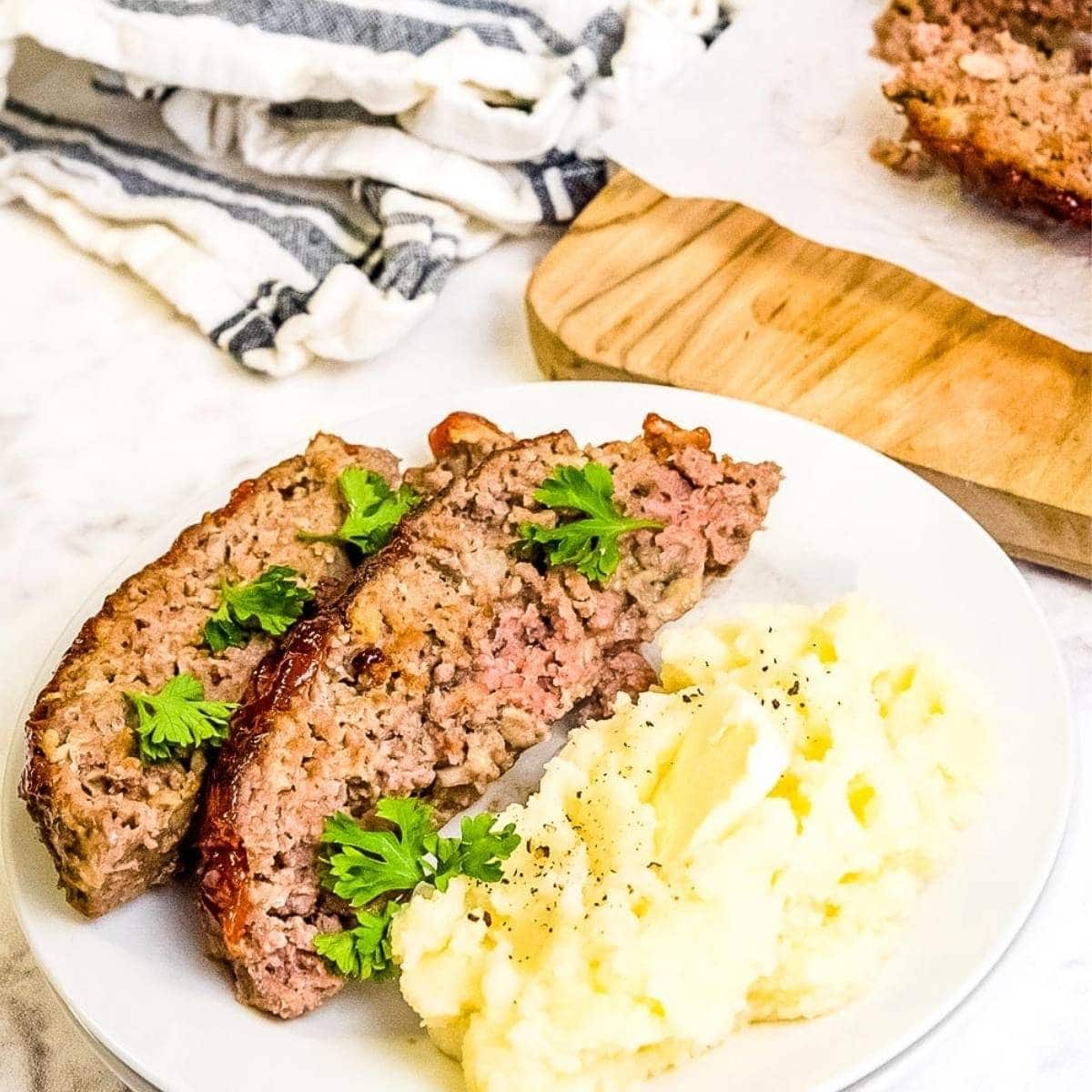 Two slices of air fried meatloaf with mashed potatoes on a white plate.