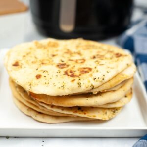 Stack of air fryer naan bread with garlic butter on a white plate.