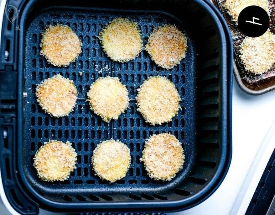 Breaded zucchini slices in air fryer basket.