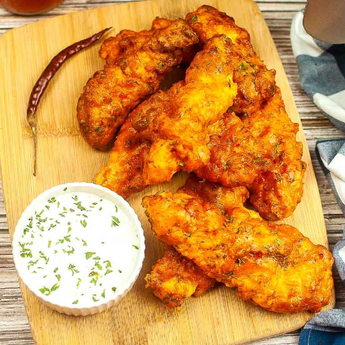 Overhead view of air fryer buffalo chicken tenders on a cutting board with a bowl of dipping sauce.