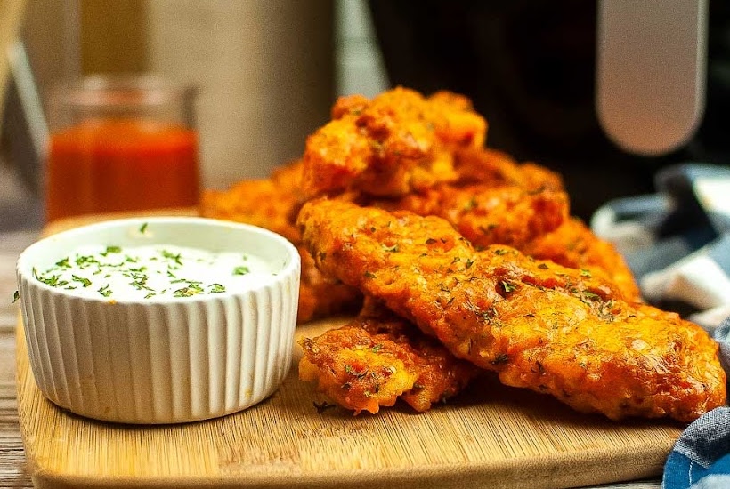 Front view of air fryer buffalo chicken strips next to a bowl of dipping sauce on a wooden cutting board.