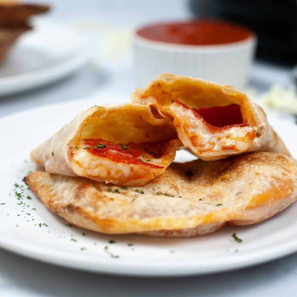 Air fried calzones on a white plate with one of them cut in half.