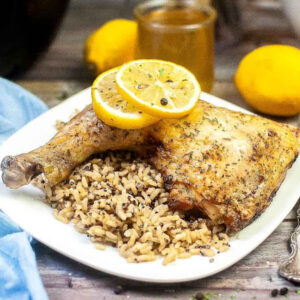 Closeup view of air fried chicken quarters with rice and lemon slices on a white plate.