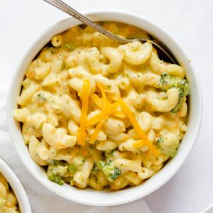 An overhead view of Panera Broccoli Cheddar Mac and Cheese in a small white bowl with a spoon inserted.
