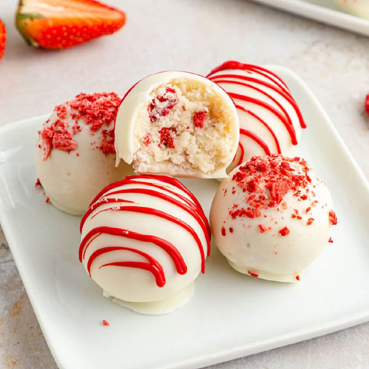 Strawberry Cake Balls on a small white plate with a bite taken from one truffle.