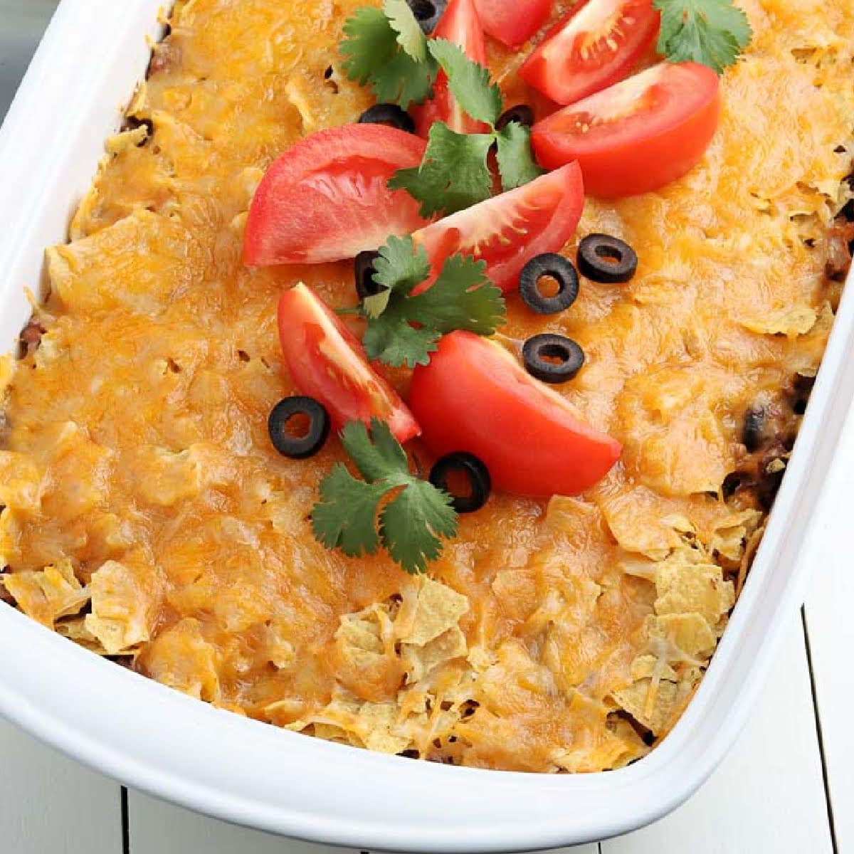 Overhead view of Walking Taco Casserole in a 9x13 white baking dish and garnished with chopped tomatoes and black olives.