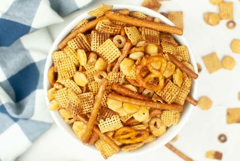 Overhead view of homemade Chex mix in a white bowl next to a blue and white towel.