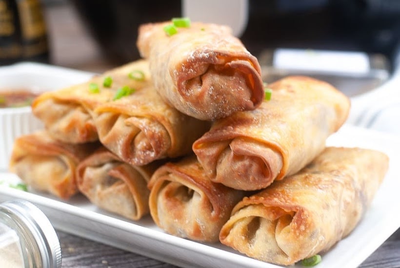 Air fried pork egg rolls stacked on a white platter.