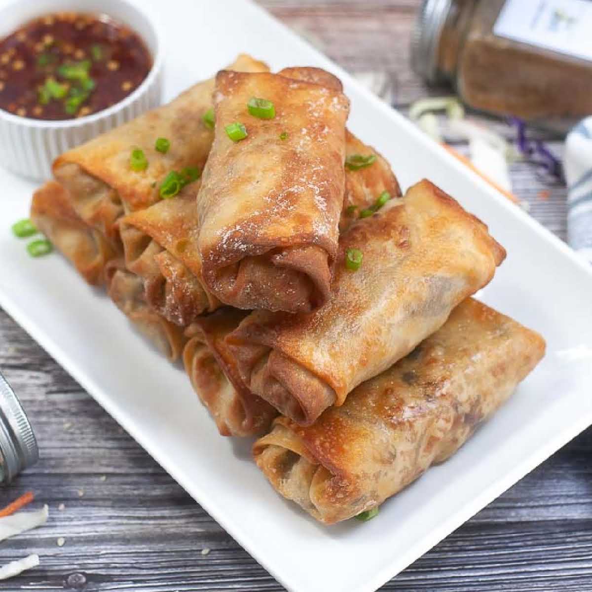 Close up overhead view of air fryer pork egg rolls garnished with chopped green onions on a white platter.
