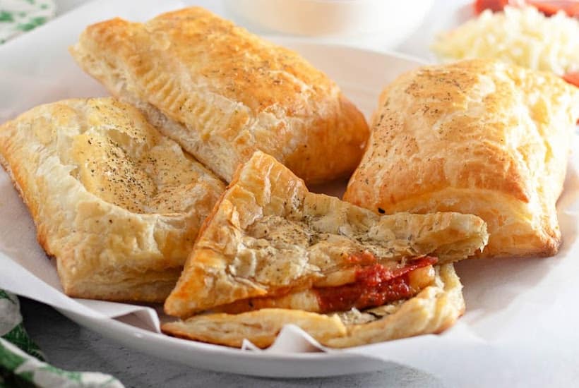 Homemade puff pastry hot pockets with pizza fillings on a parchment lined white plate with one cut in half.