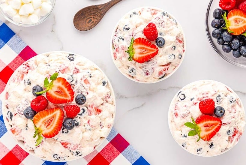 Overhead view of three bowls of berry cheesecake fluff salad on a white background.