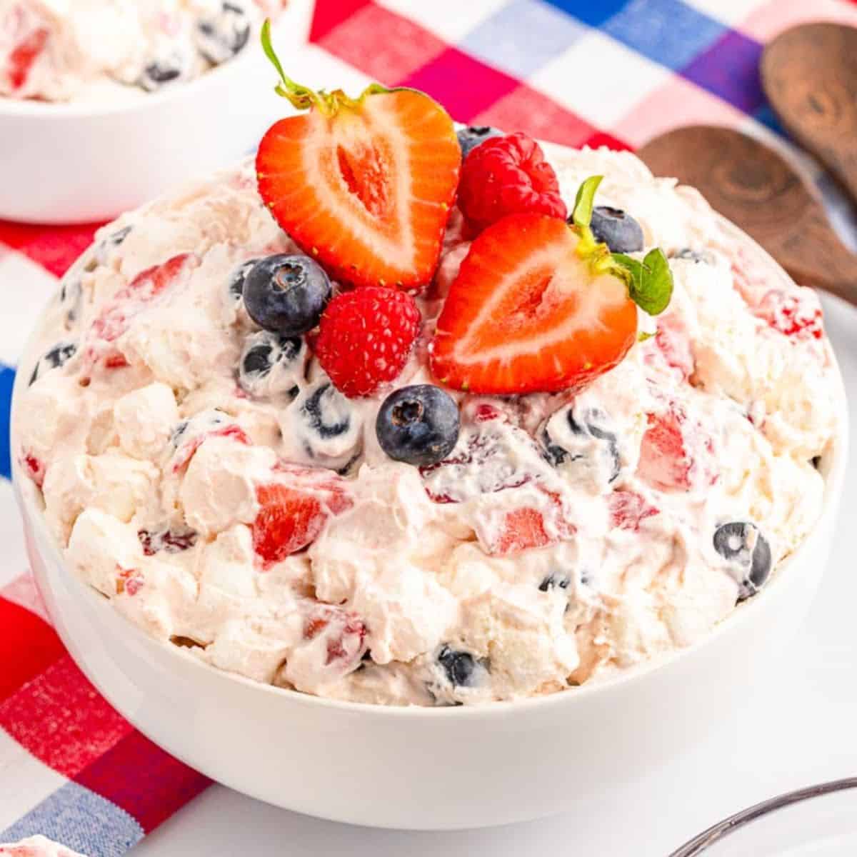 Front close up view of Red White and Blue Cheesecake Salad in a white bowl and garnished with fresh berries.