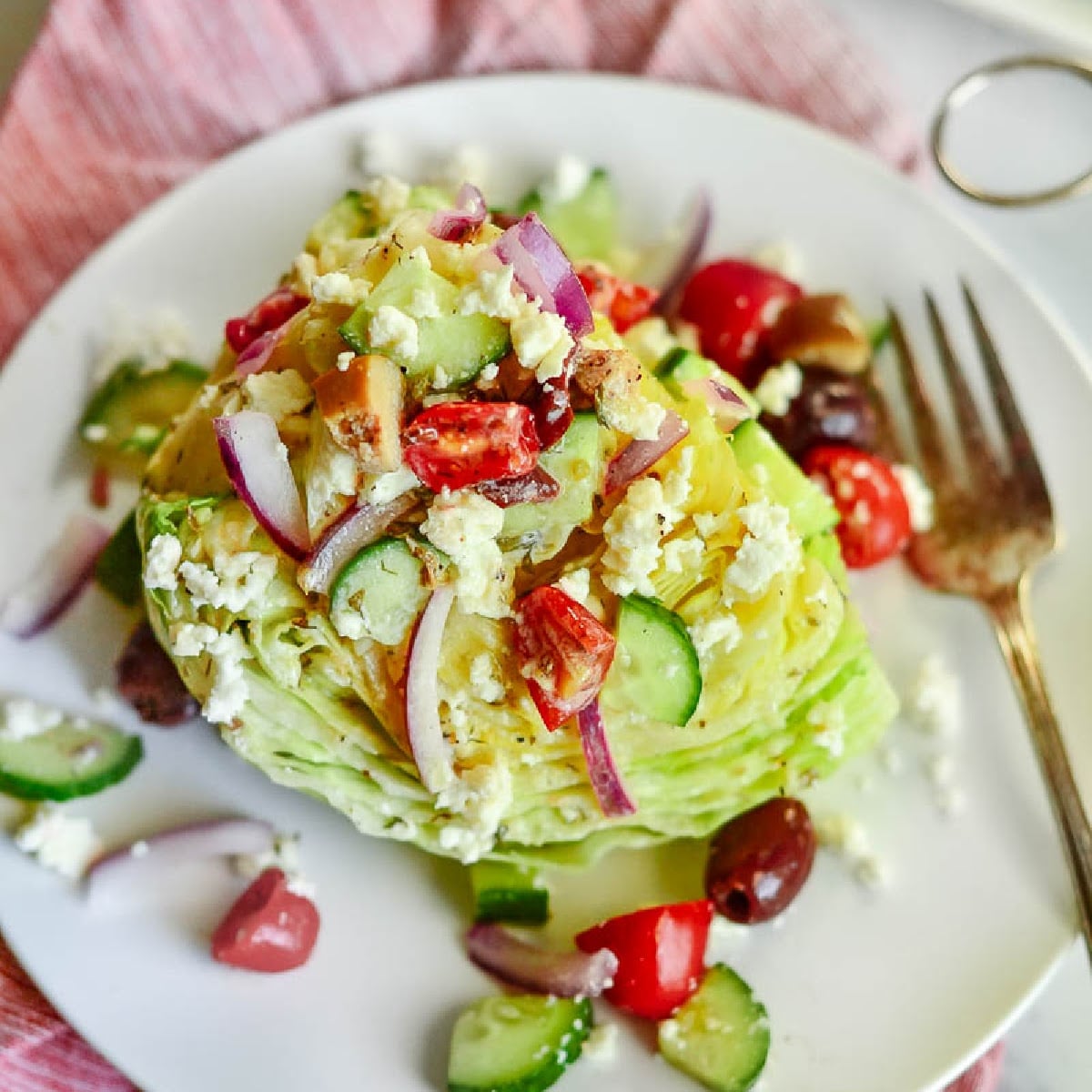 Overhead view of Mediterranean Wedge Salad on a white plate with a fork.