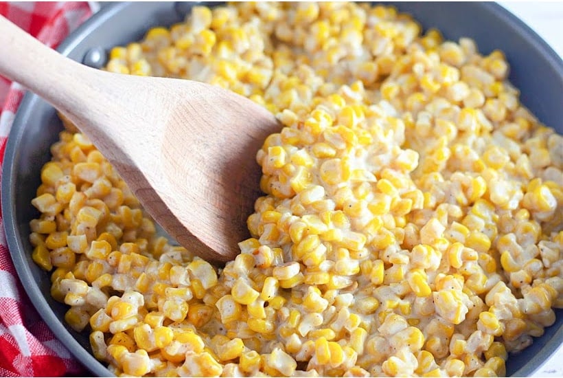Homemade skillet creamed corn with cream cheese and a wooden spoon in a pan.