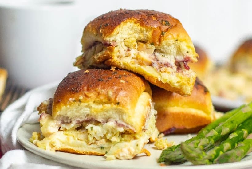 Holiday Leftover Thanksgiving Sliders stacked on each other on a plate next to asparagus.