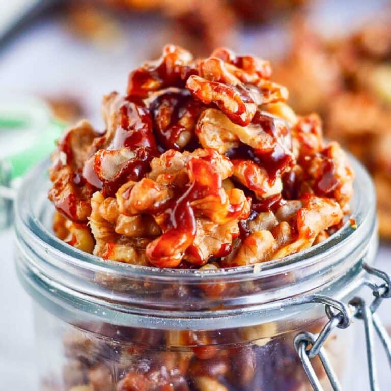 Close up of a clear jar filled with brown sugar candied walnuts.